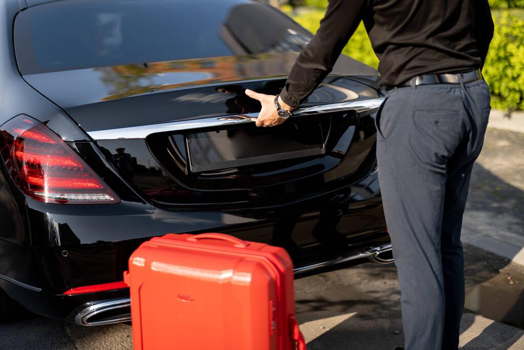 Chauffeur packing red suitcase in car trunk