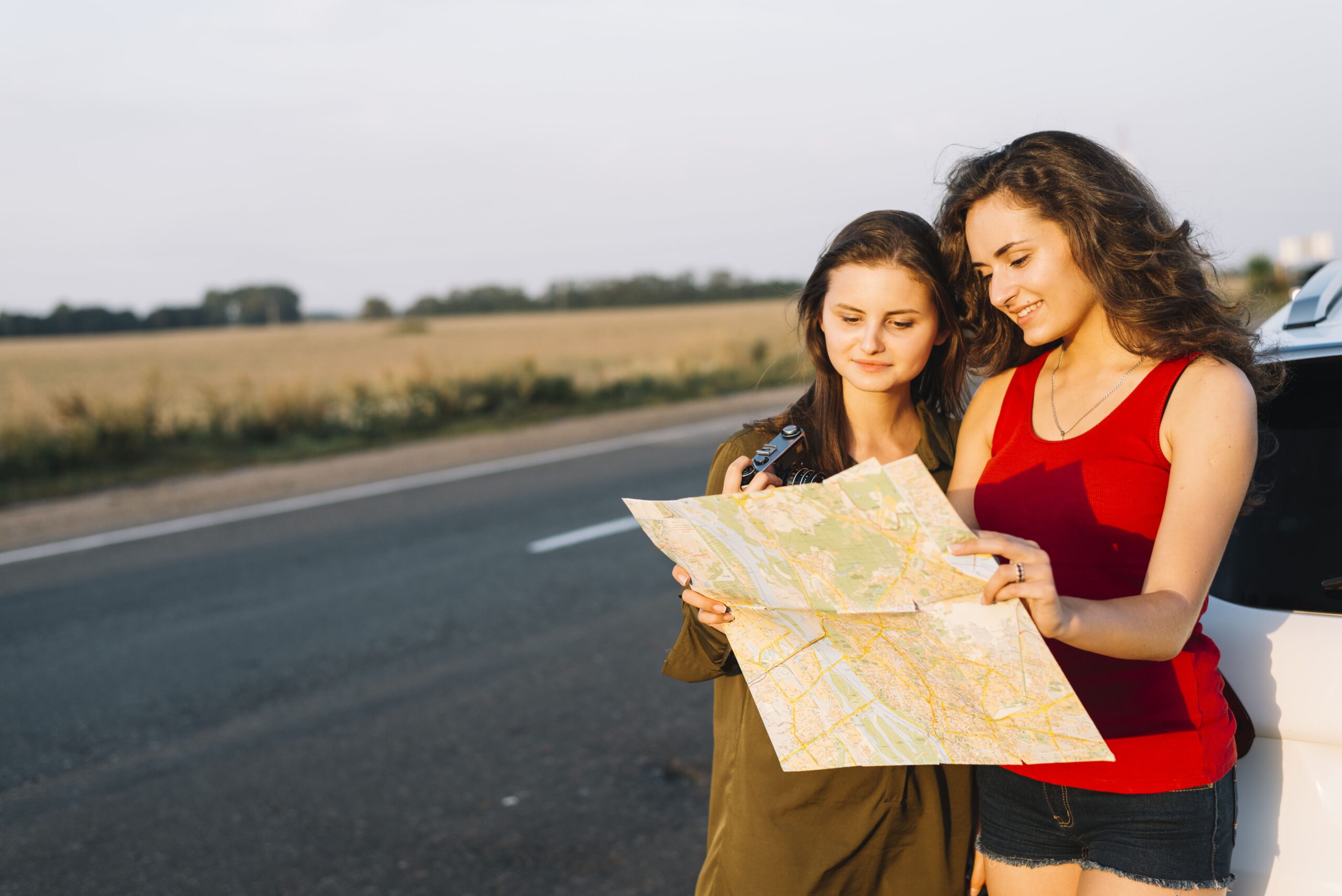 Women standing near white car and looking at map