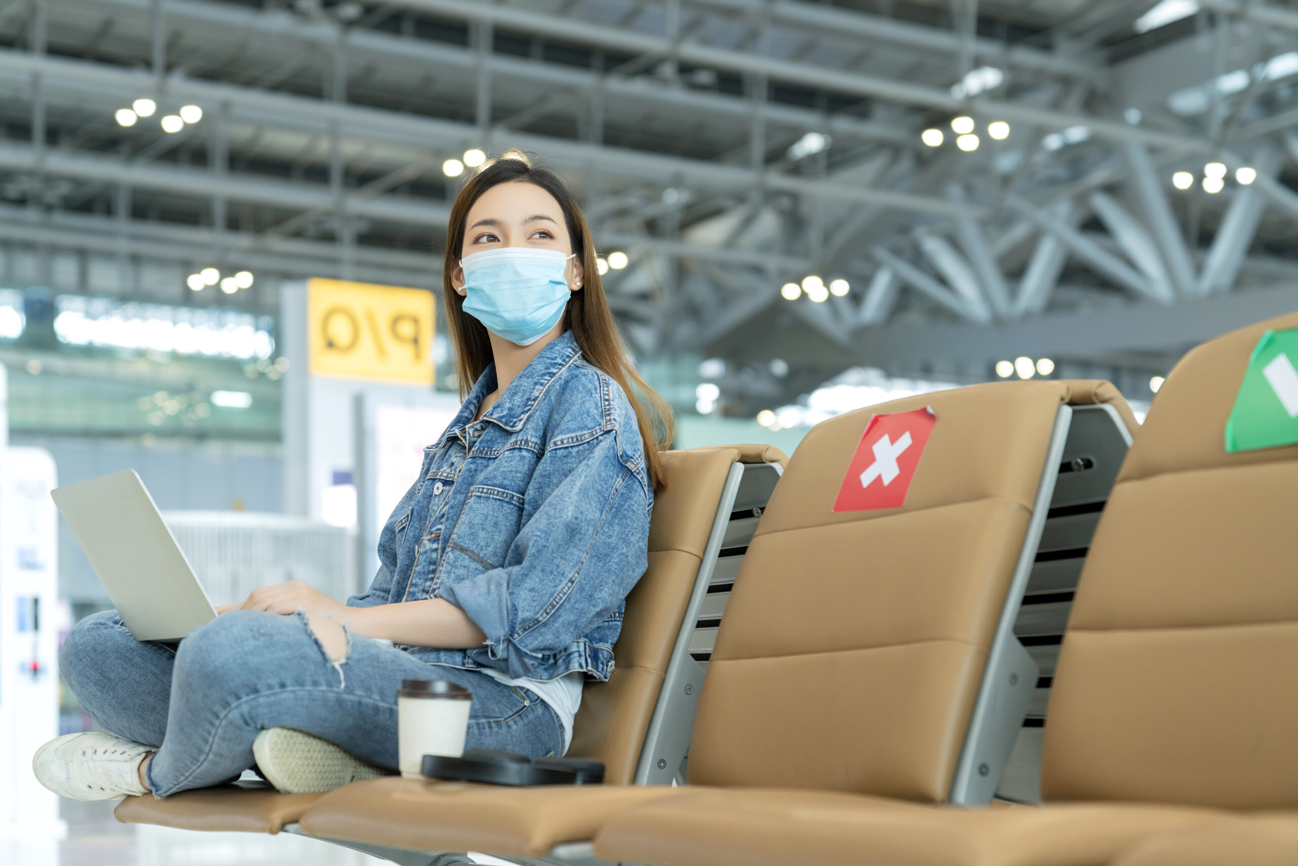 Social distancing, businesswoman wearing face mask sit working with laptop keeping distance away from each other to avoid covid19 infection during pandemic. Empty chair seat red cross shows new normal